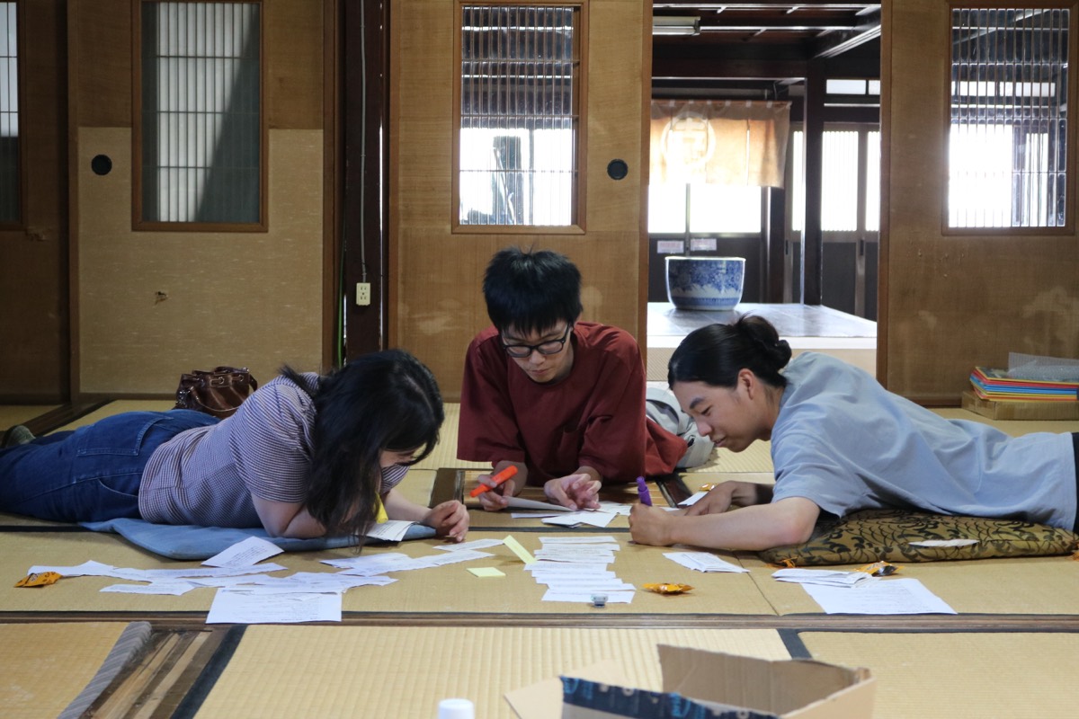 3人の参加者が畳に寝そべり、カードに色ペンで線を引いている